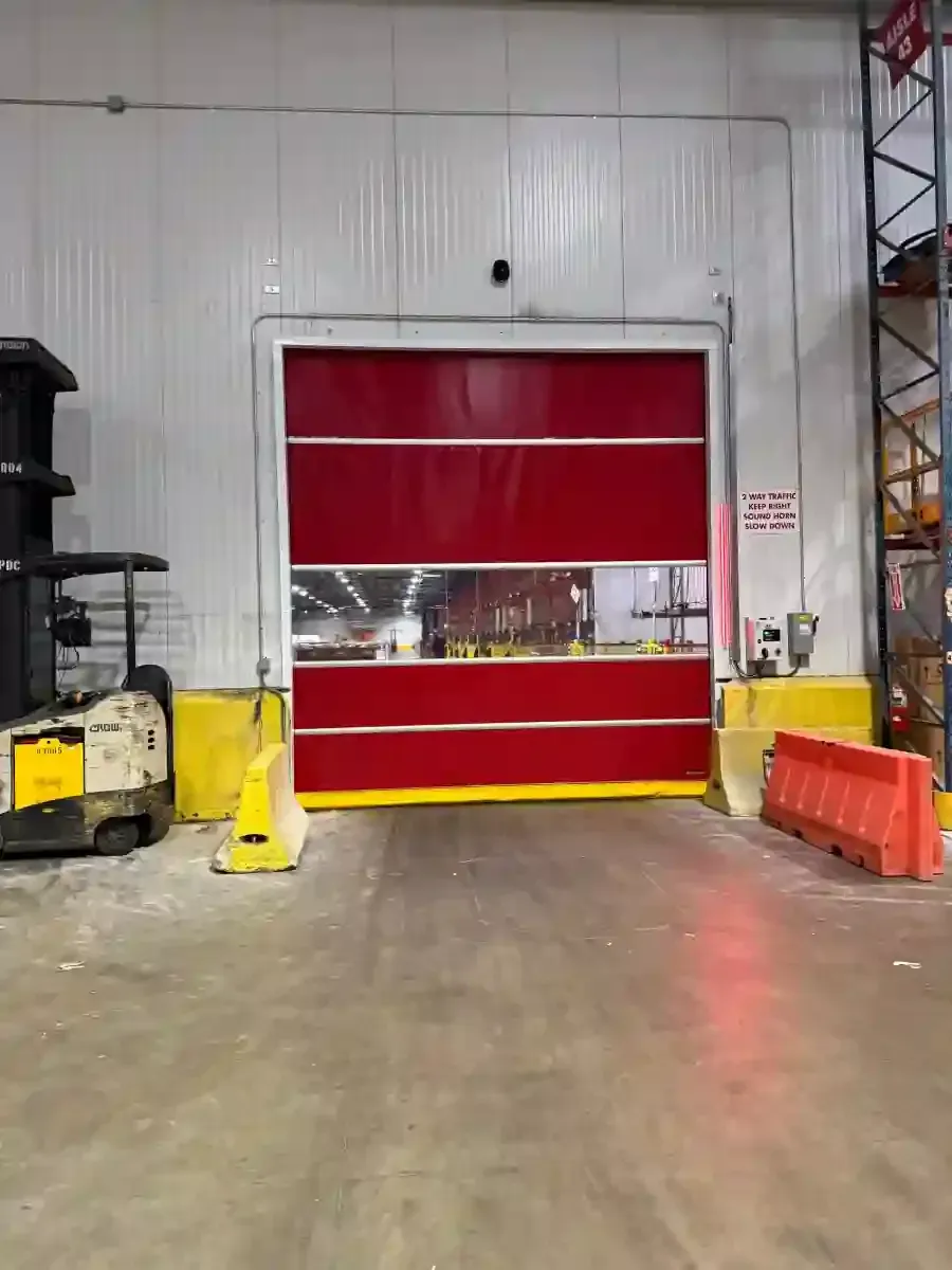 Industrial warehouse bay with a red roll-up door, concrete floor, and safety barriers on both sides