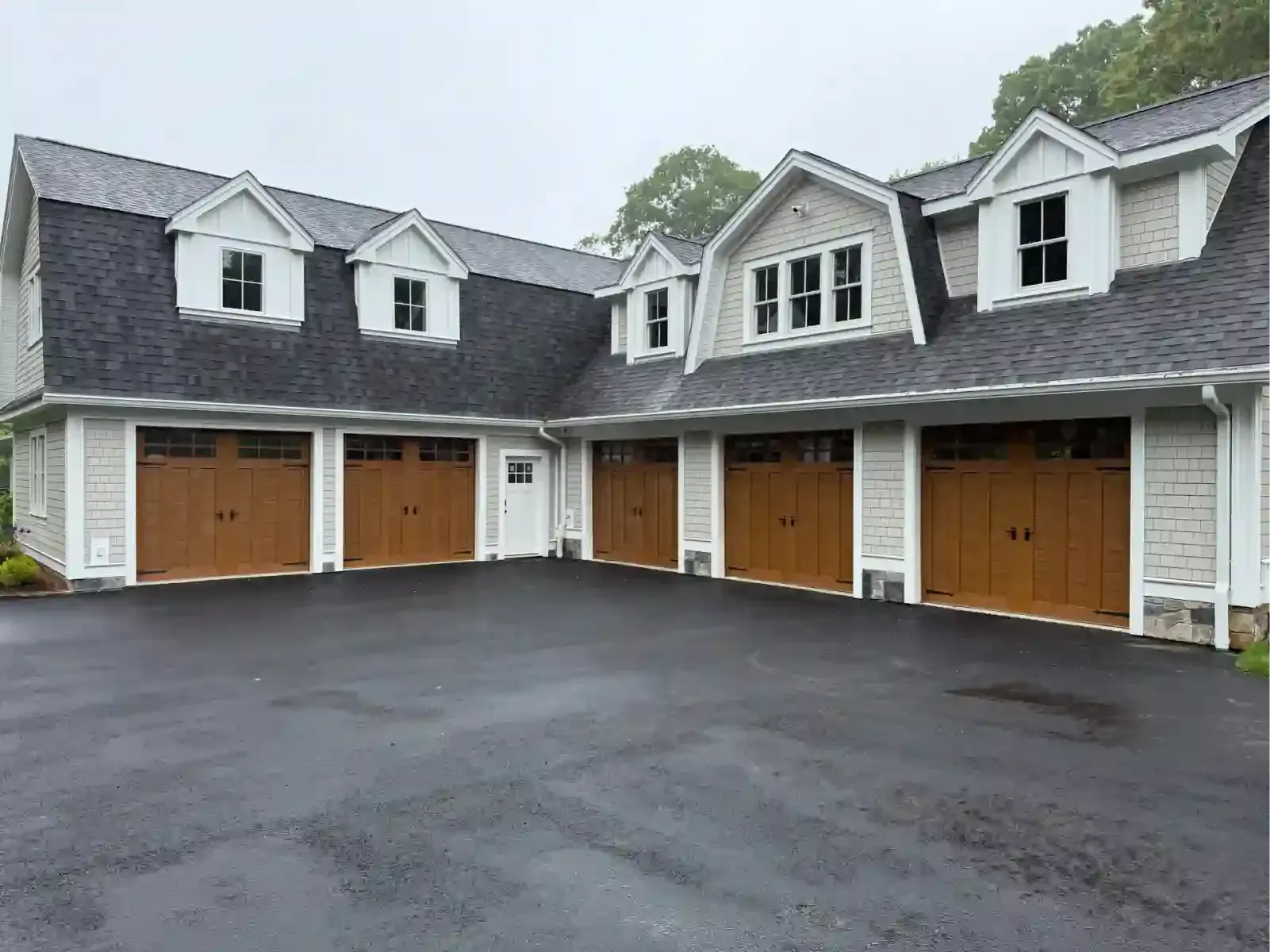 Row of attached garage doors on a gray townhouse with a wet blacktop driveway