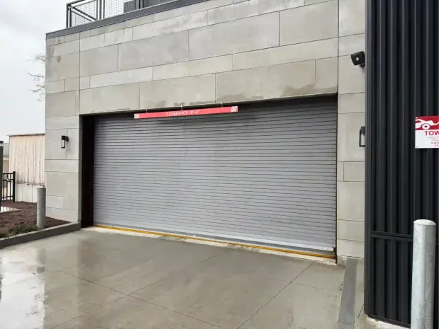 Closed gray garage door on a light stone building with a wet concrete driveway