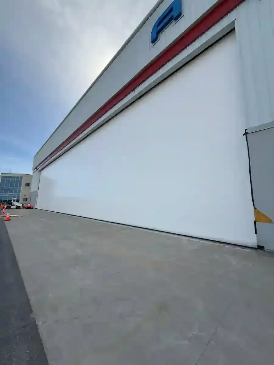 Large white warehouse exterior with a red stripe beside a wide concrete lot under a cloudy sky