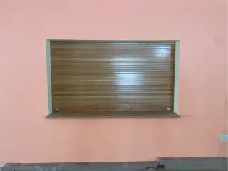 Closed wooden shutter on a pink wall with a gray trim and ledge below.