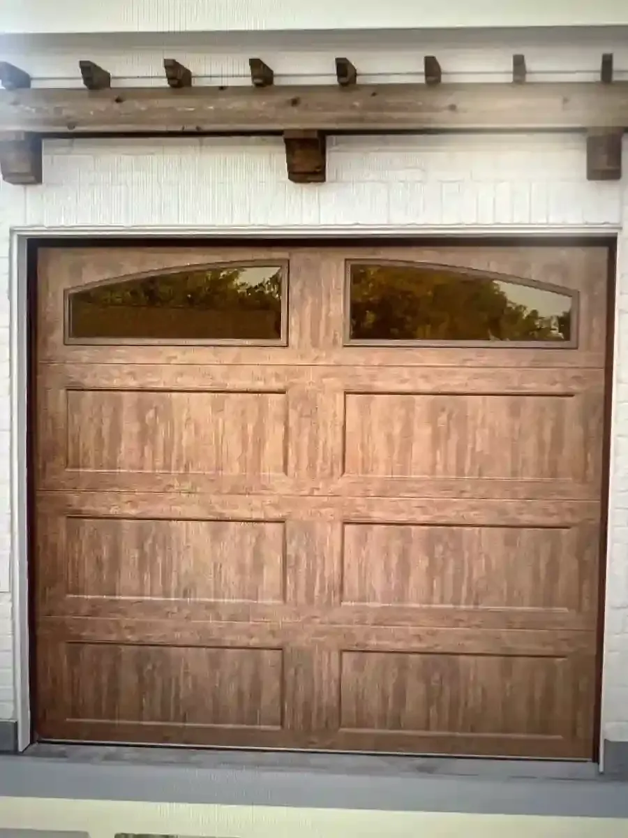 Wooden double garage door with small trapezoid windows under a white stucco overhang