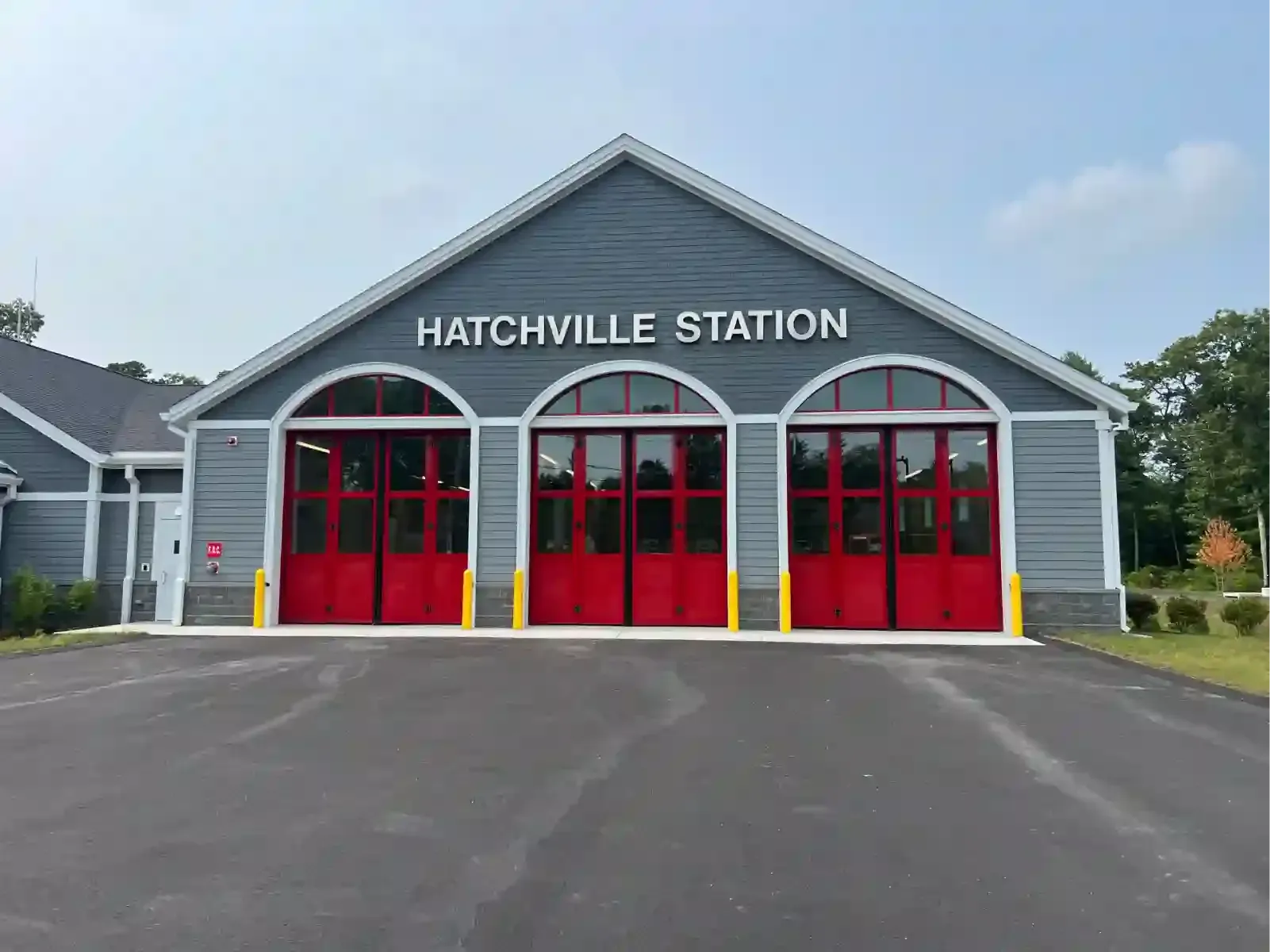 Hatchville Station building with gray siding and bright red garage doors under a blue sky