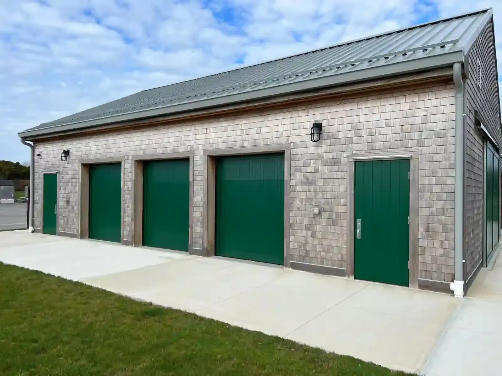 Brick storage building with four green garage doors and one side door on a concrete pad.