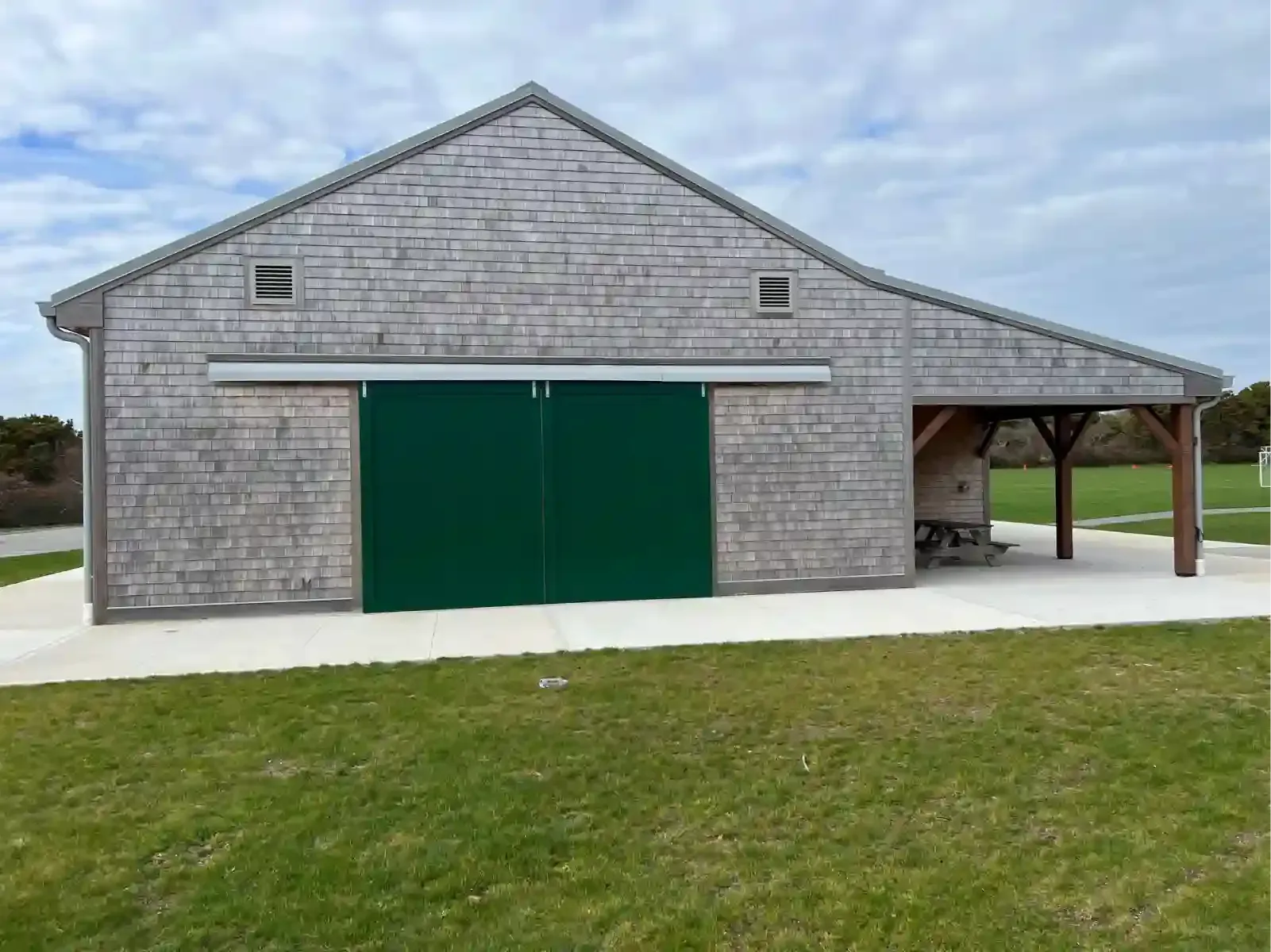 Brick building with large green doors and a covered side porch on a grassy lot