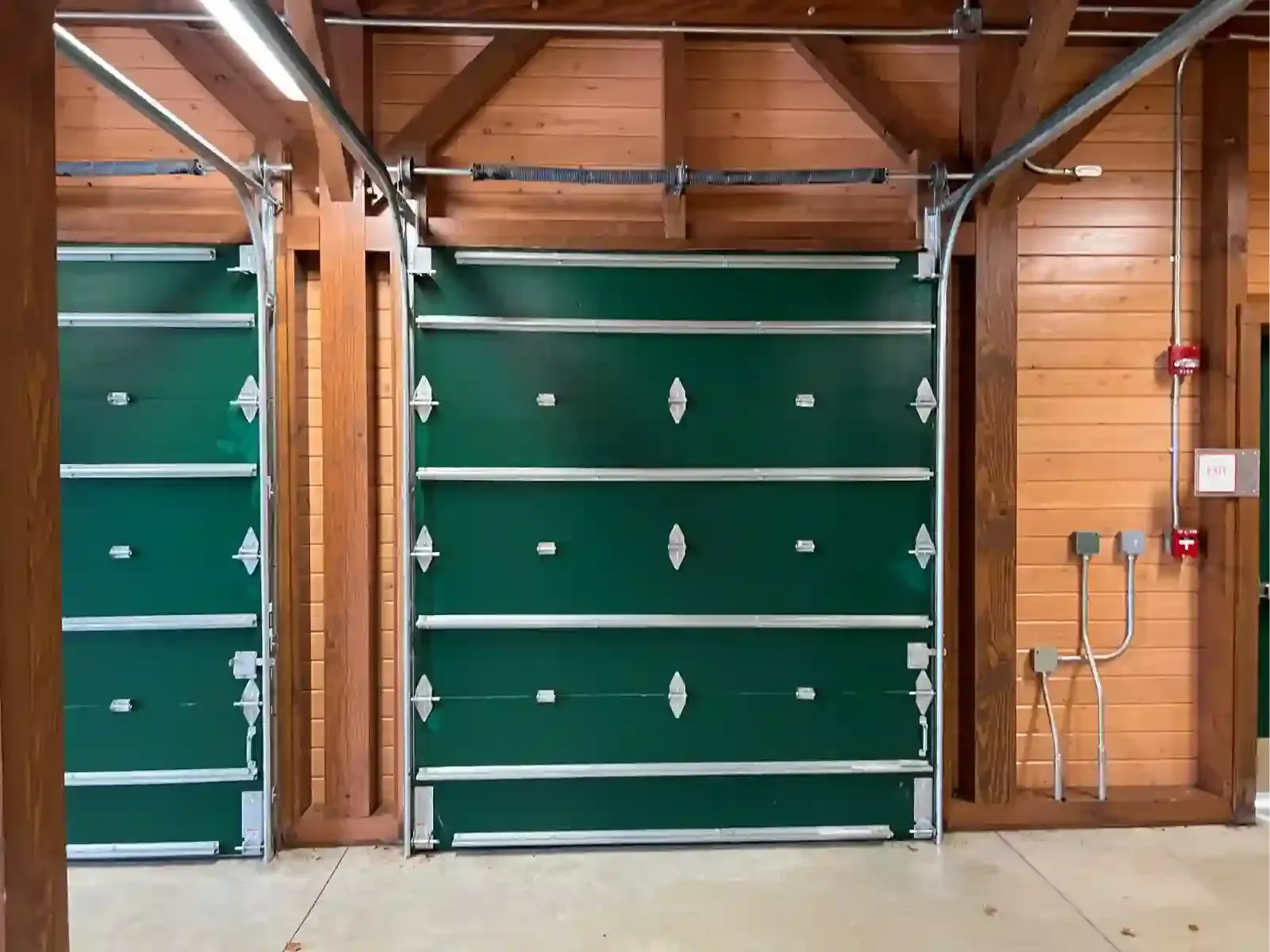 Three green garage doors in a wooden-framed interior with overhead beams and a concrete floor