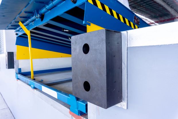 Blue industrial machine with yellow accents and a gray block inside a factory setting
