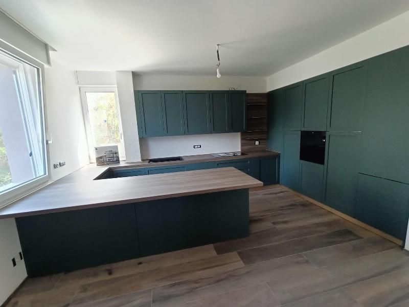 Cucina moderna con mobili color verde acqua, pavimento in legno e un'ampia isola vicino a luminose finestre.