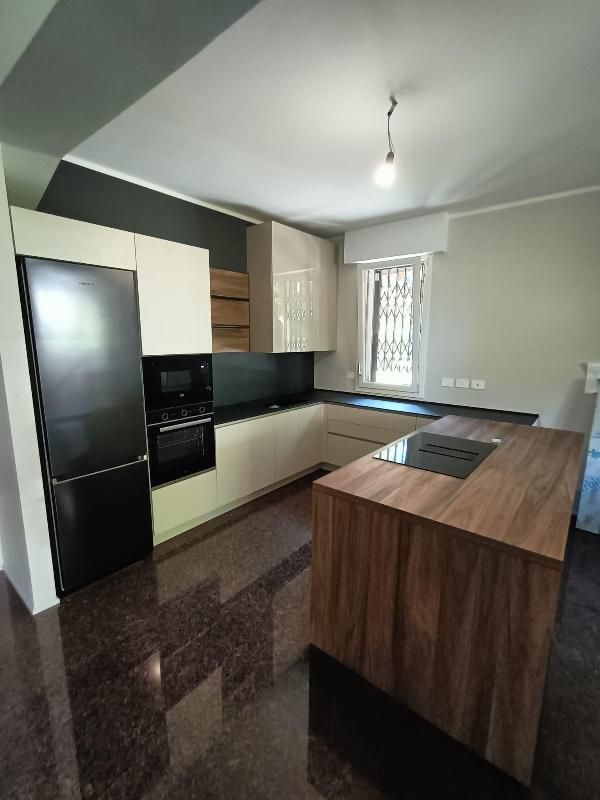 Cucina moderna con elettrodomestici neri, isola in legno, mobili beige e una finestra che lascia entrare la luce naturale.