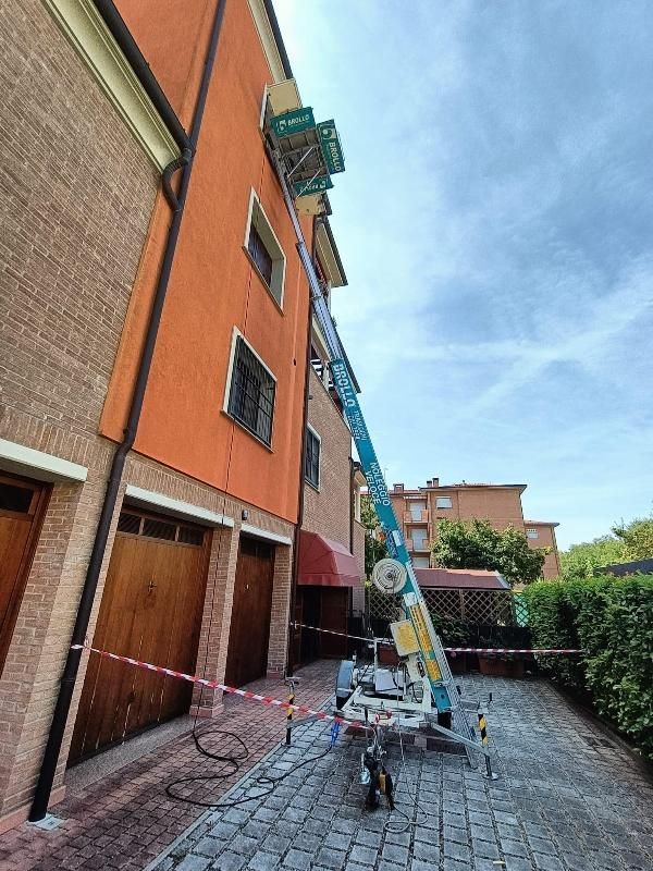 Un operaio su una piattaforma elevatrice ripara il tetto di un condominio arancione in uno stretto cortile.