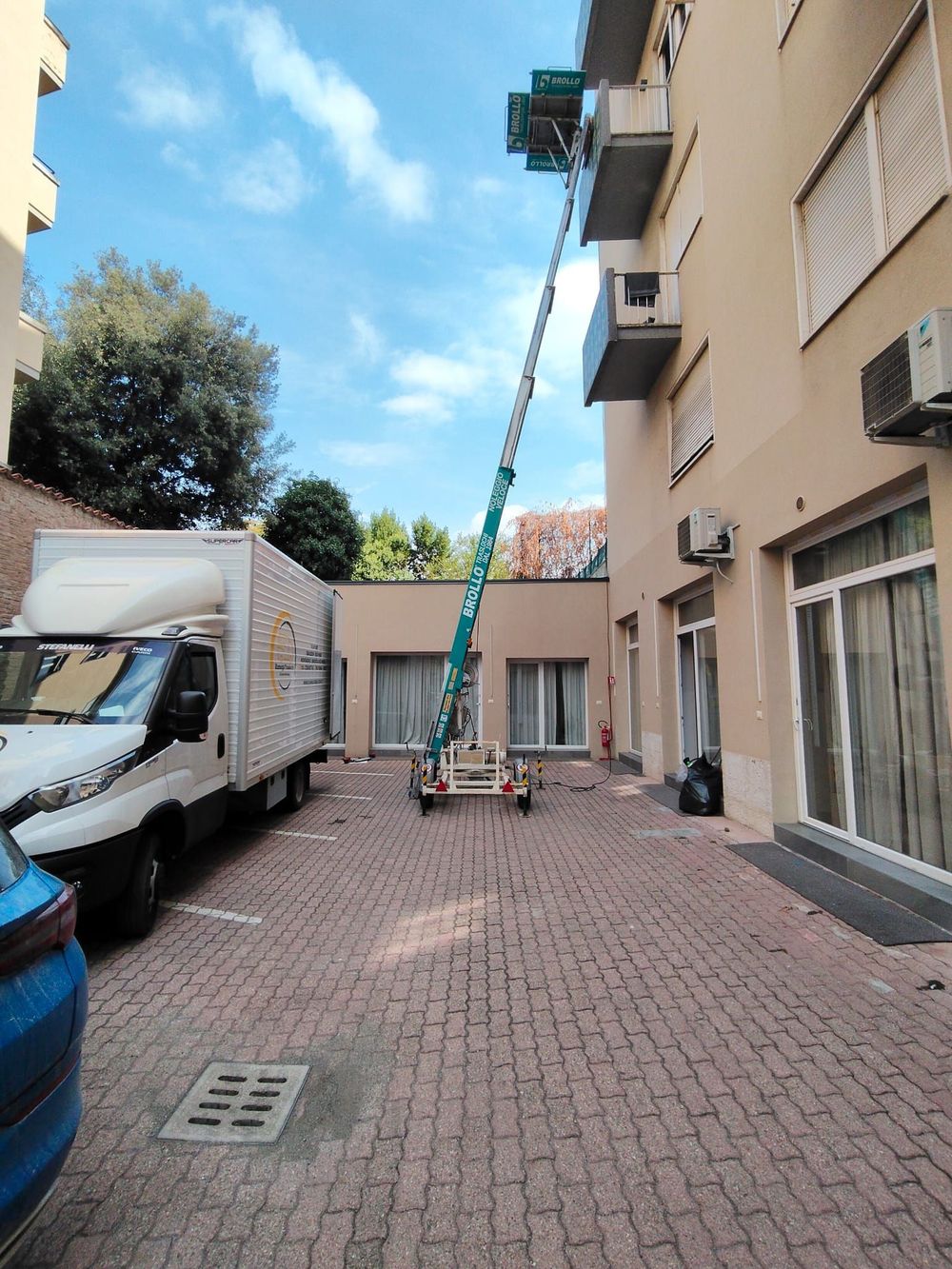 Un operaio su una piattaforma aerea accanto a un edificio arancione con garage e un cortile lastricato.