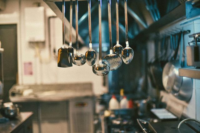 Utensili da cucina appesi sopra i fornelli, con pentole e padelle in acciaio inossidabile visibili sullo sfondo.