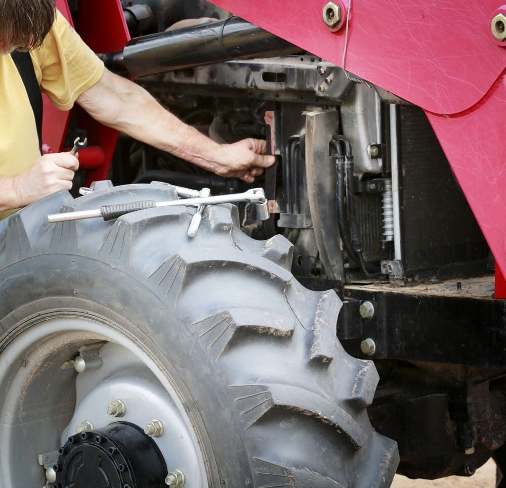A Man In A Yellow Shirt Is Working On A Red Tractor — Leslie Farm & Garden Machinery In South Grafton, NSW