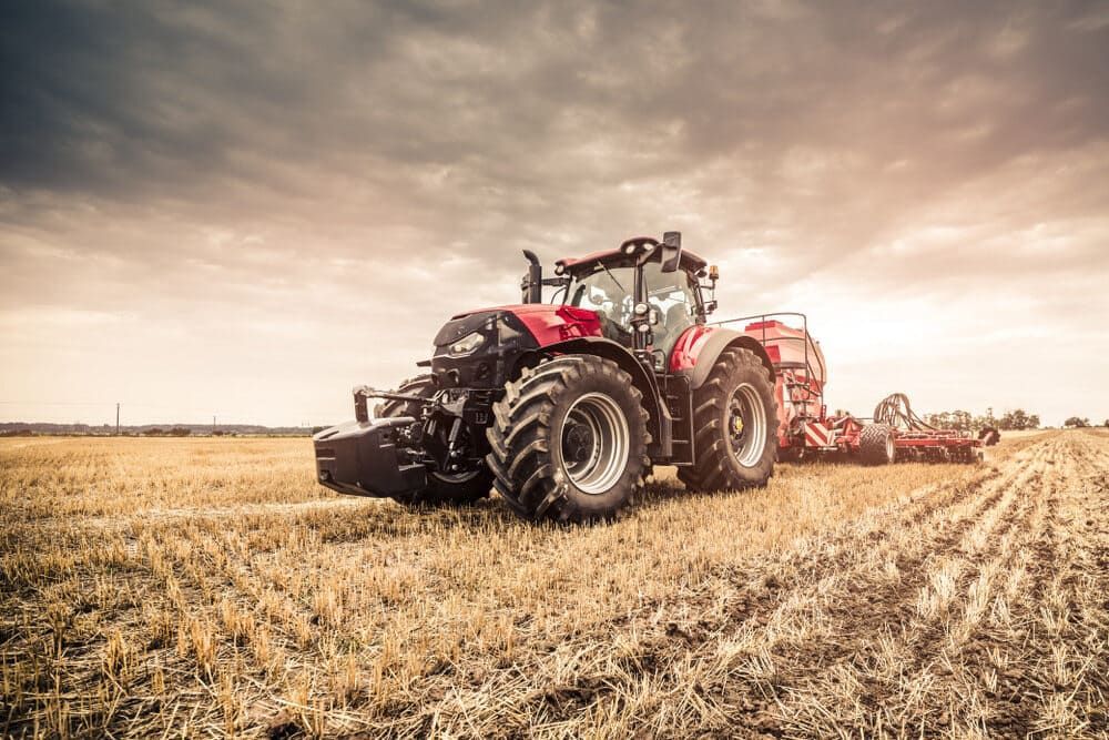 A Red Tractor Is Plowing A Field At Sunset — Leslie Farm & Garden Machinery In South Grafton, NSW