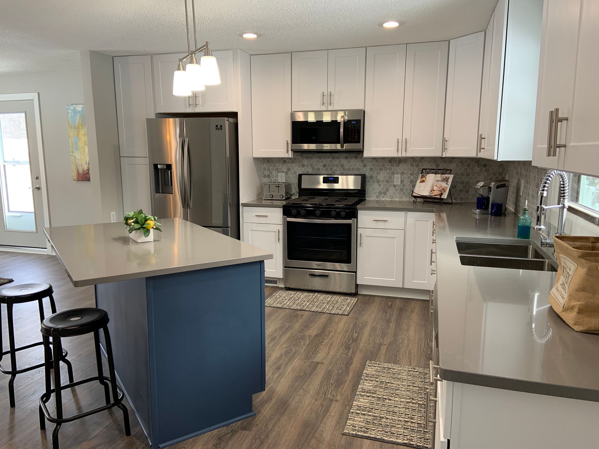 Modern kitchen with stainless steel appliances, white cabinets, blue island, and wood-look floors