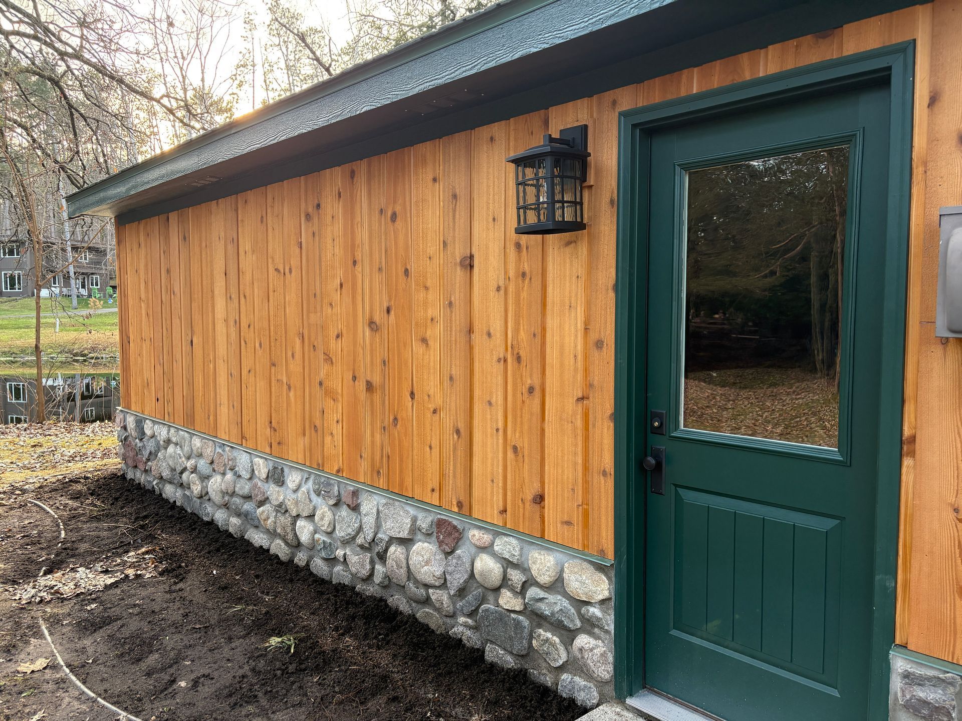 A green-trimmed door set into a building with vertical wooden siding and a stone foundation base.