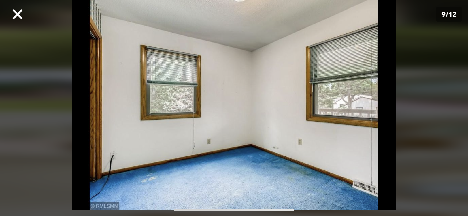 Empty room with blue carpet, white walls, and two small windows with blinds and framed shades.