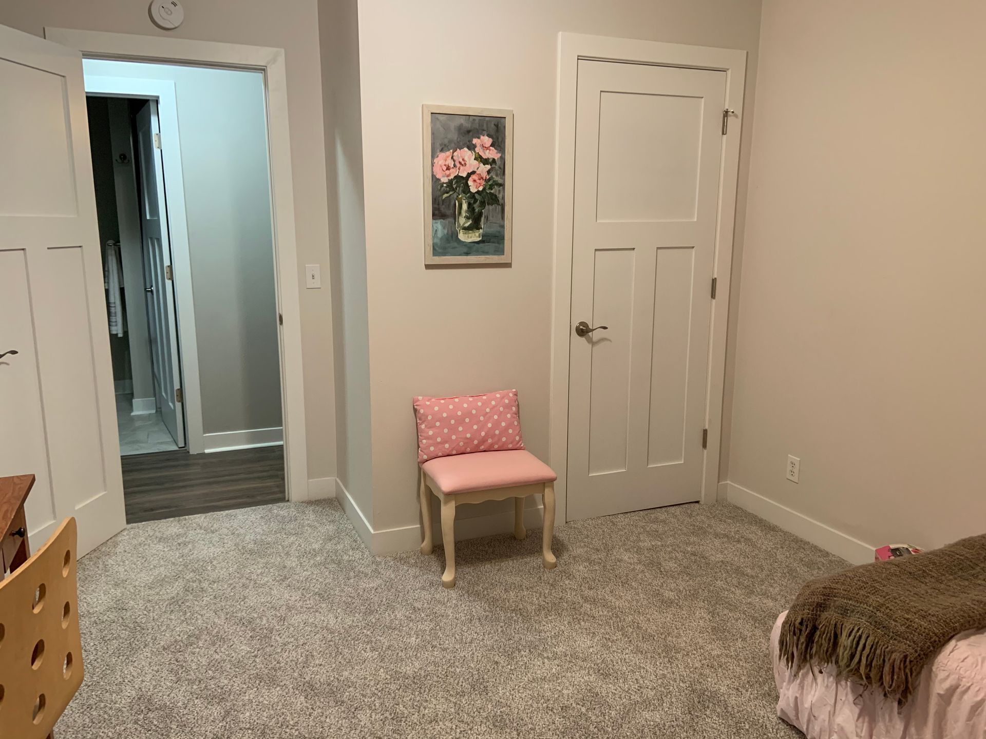 Bedroom with beige walls, two doors, a pink chair, floral wall art, and carpeted floor.