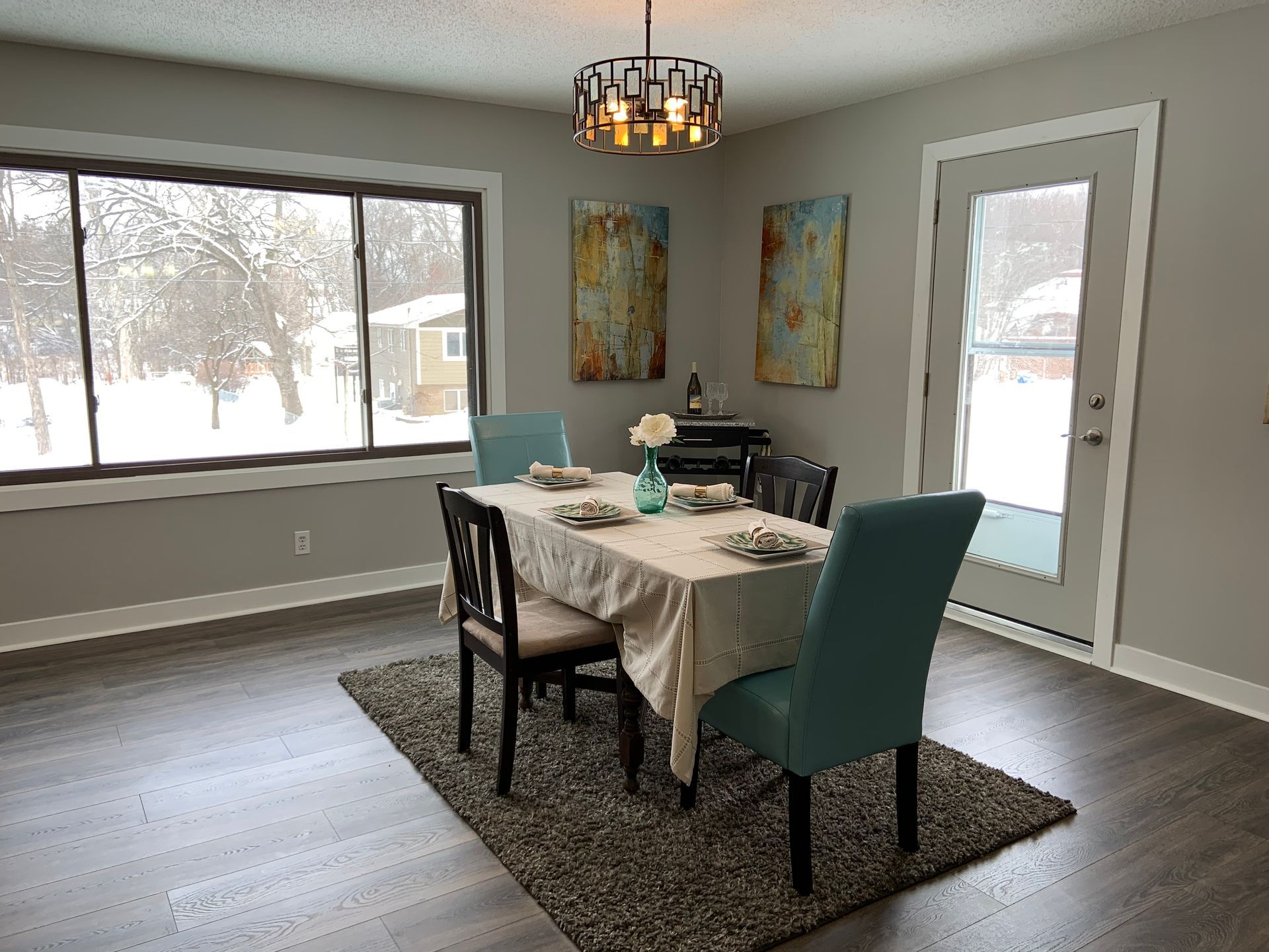 Dining room with a table, chairs, art, a rug, and a large window looking out on snow.