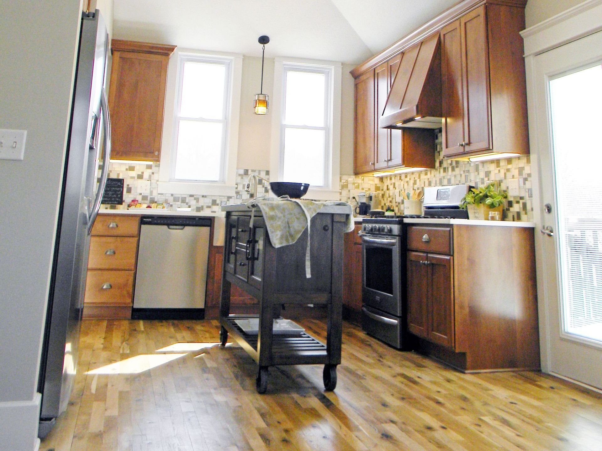 Kitchen with brown cabinets, stainless steel appliances, and island. Light wooden floors and a glass door.