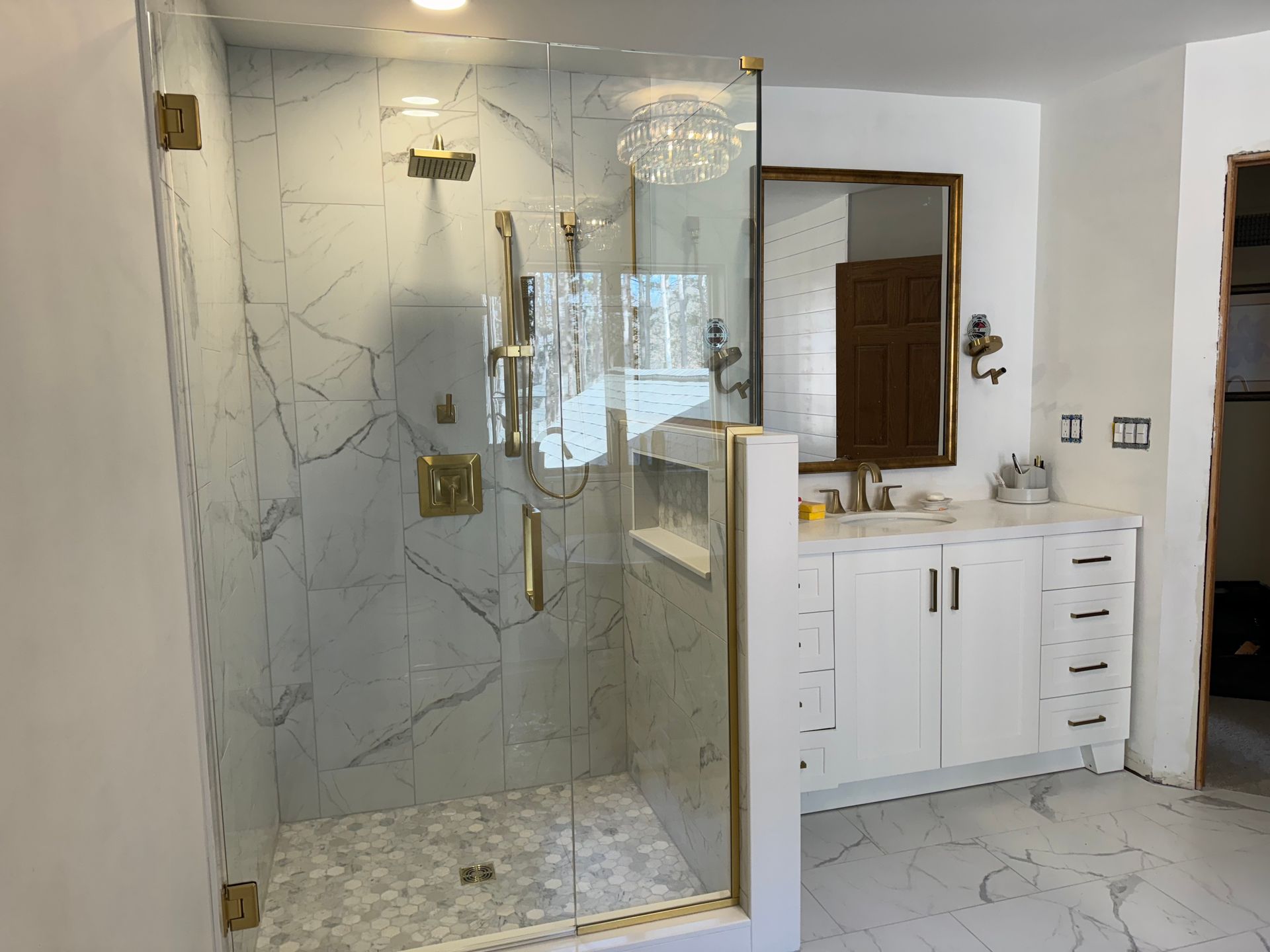 Modern bathroom with marble tile shower, gold fixtures, and white vanity.