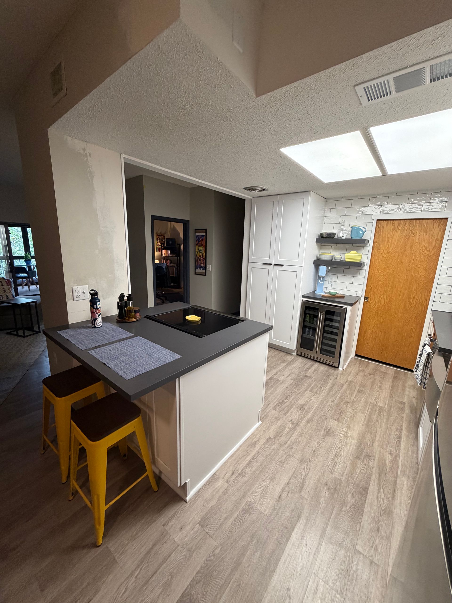 Kitchen with a gray island, yellow stools, and light wood flooring.