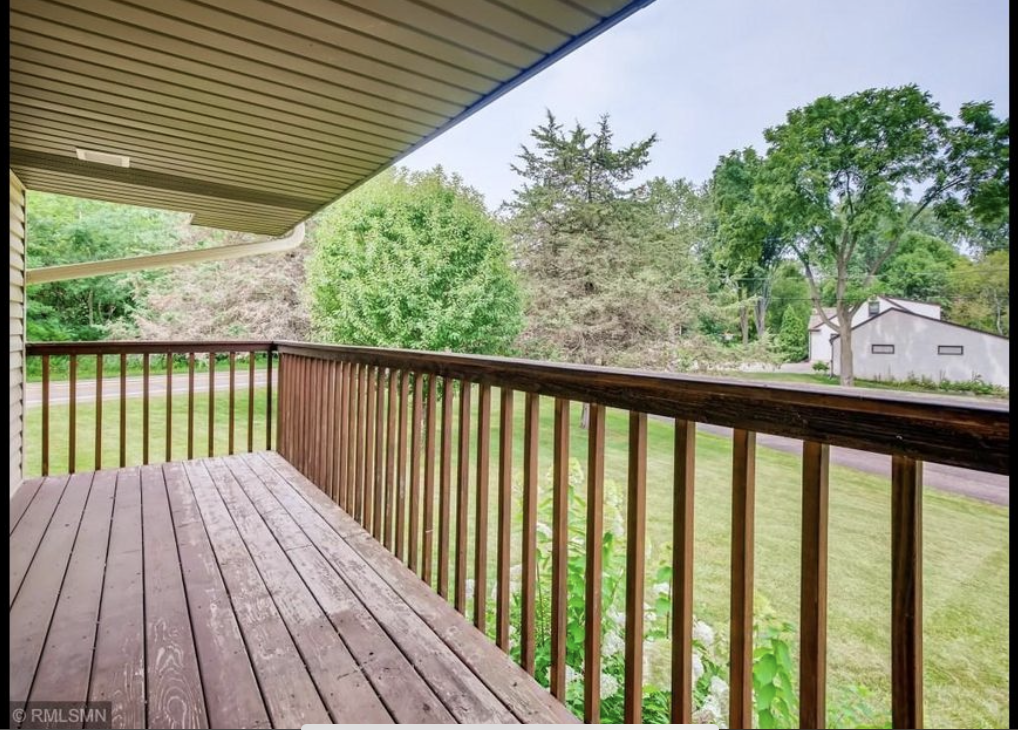 Wooden porch with railing overlooking a grassy yard with trees and a small white building.