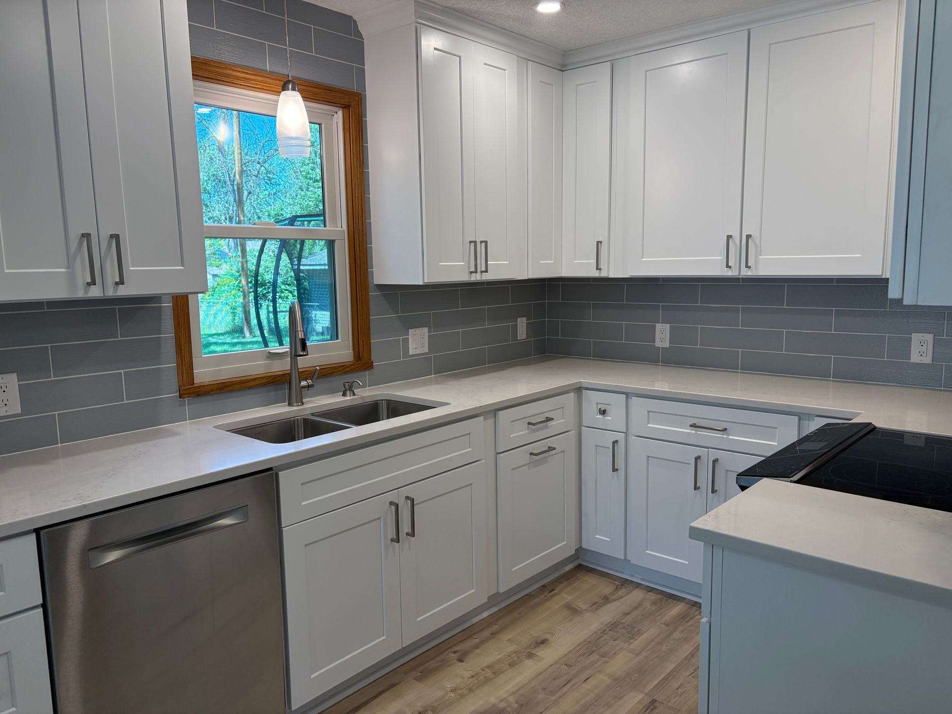 White kitchen with light countertops and gray backsplash. Stainless steel appliances.