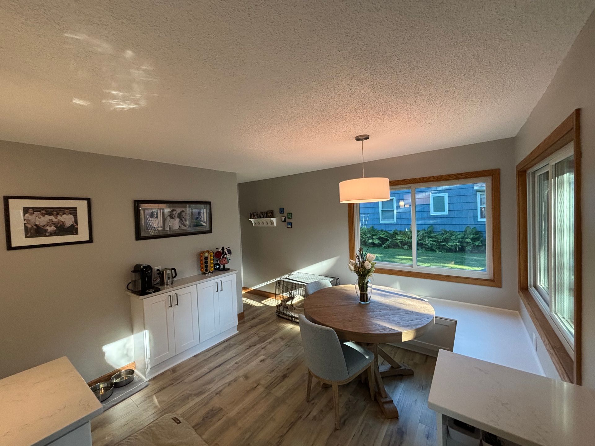 Dining room with wooden table, light blue chair, window, and white cabinets.