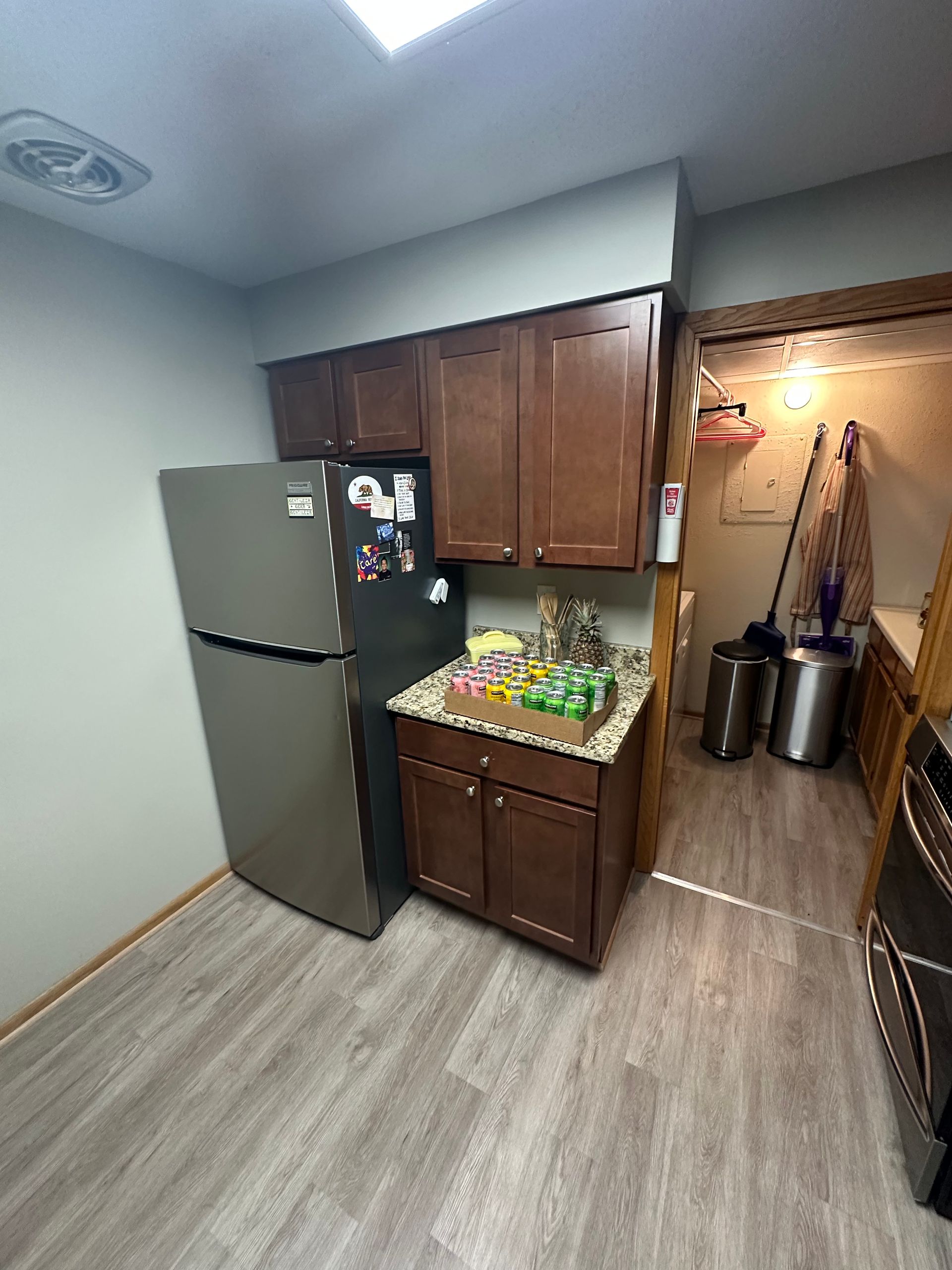 Small kitchen with brown cabinets, refrigerator, and doorway to a storage area.