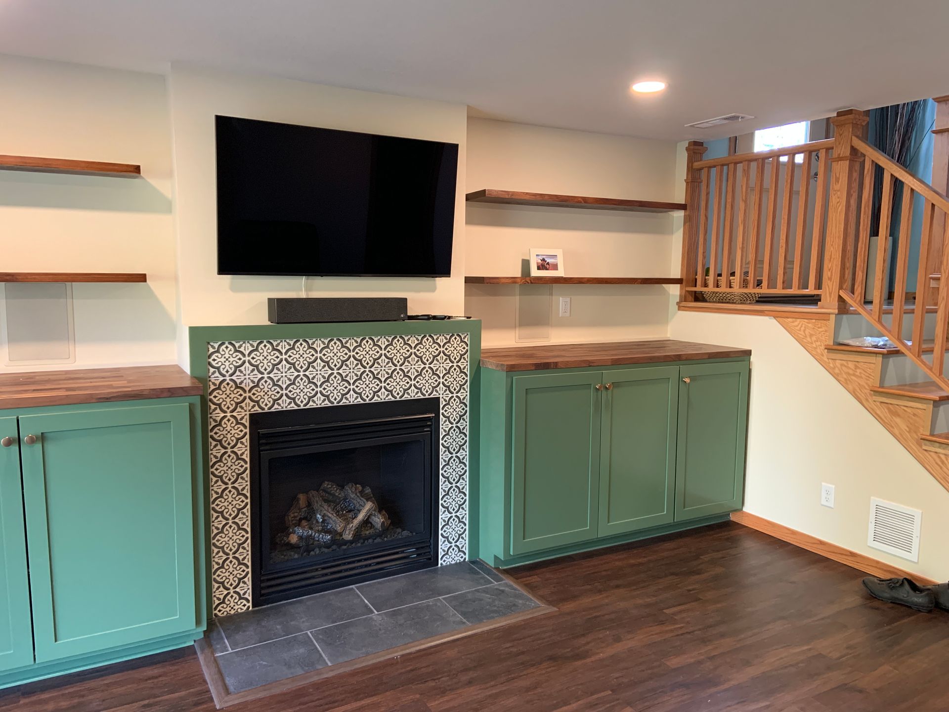 Living room with green cabinets, fireplace with decorative tile, floating shelves, TV.