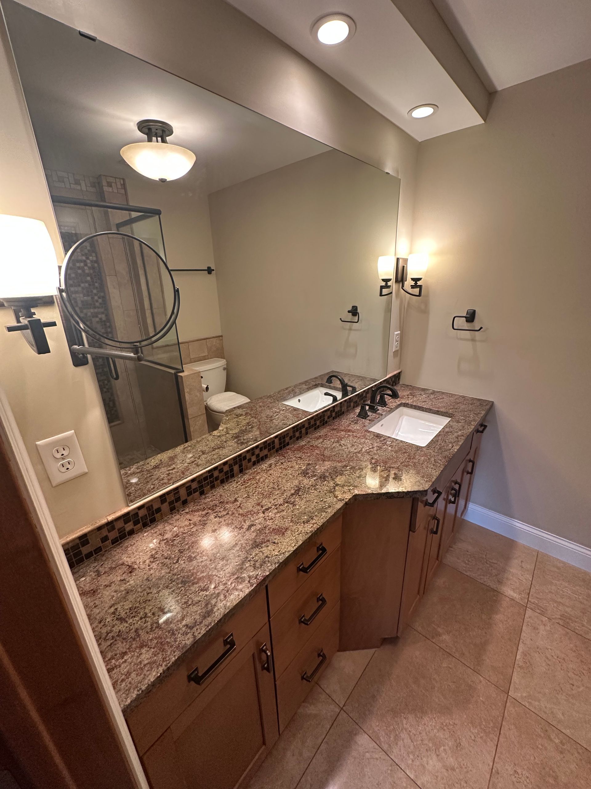 Bathroom with a large mirror, brown granite countertop, and wooden cabinets.