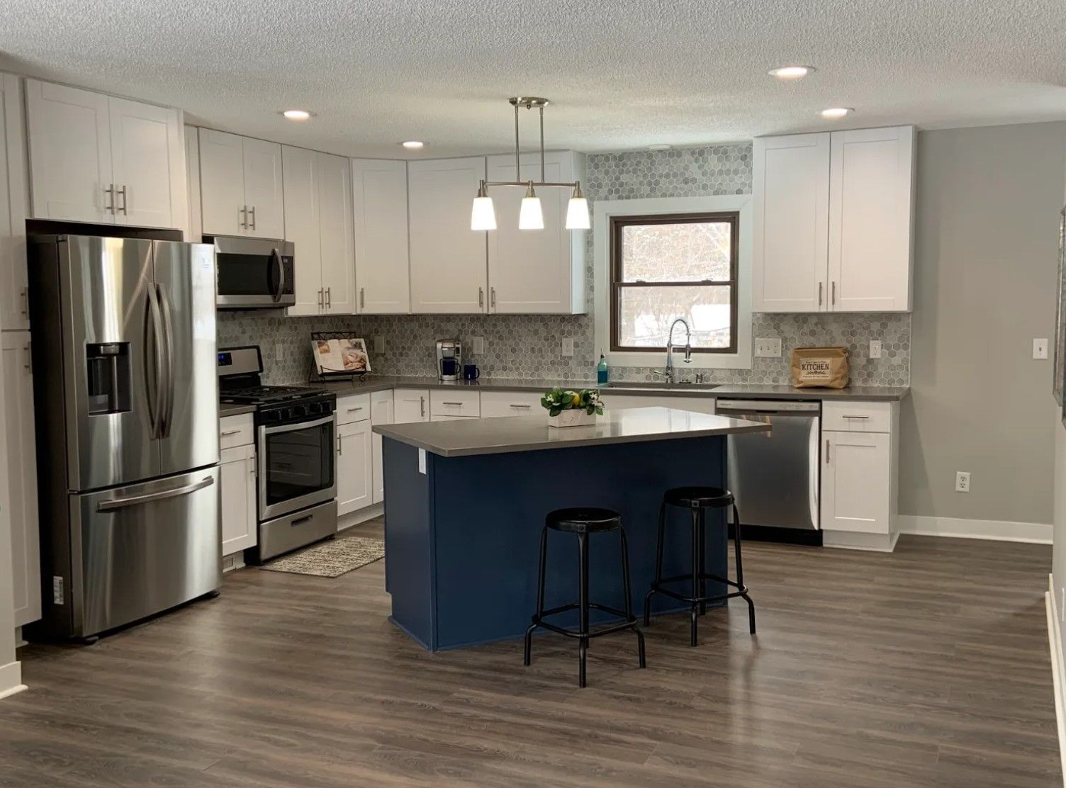 Modern kitchen with white cabinets, stainless steel appliances, blue island, and dark wood-look flooring.