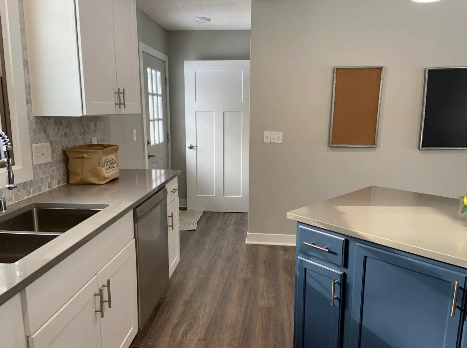 Modern kitchen with white and blue cabinets, grey countertops, and a wooden floor.