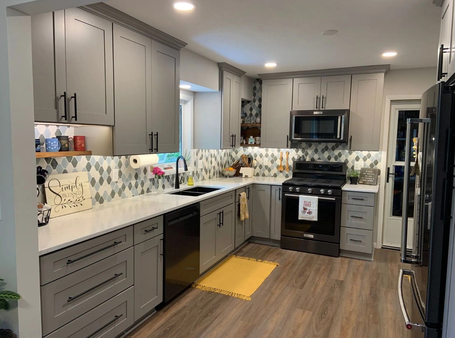 Gray kitchen with white countertops, black appliances, and patterned backsplash.