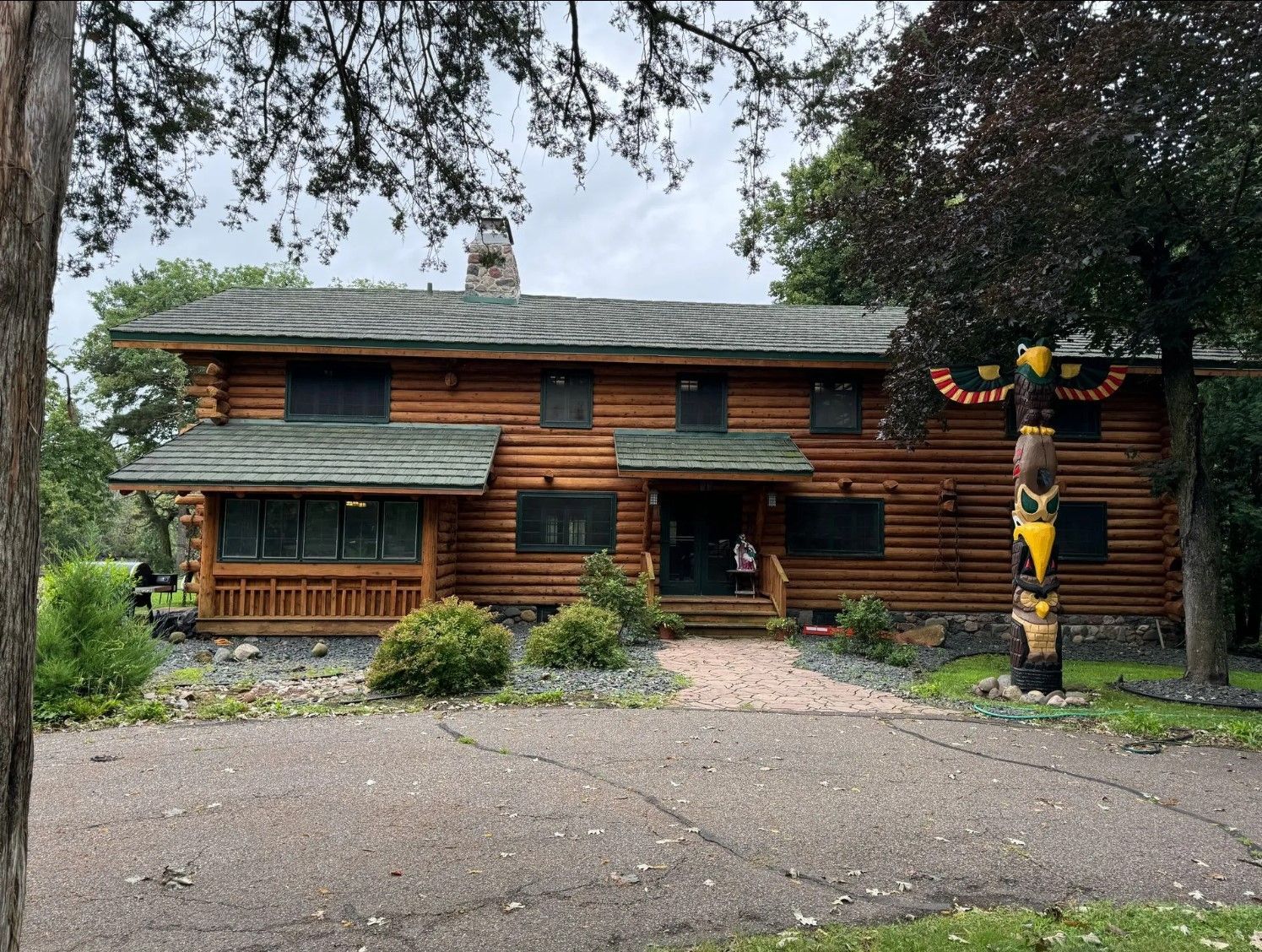 Two-story log cabin house with a paved driveway and decorated totem pole.