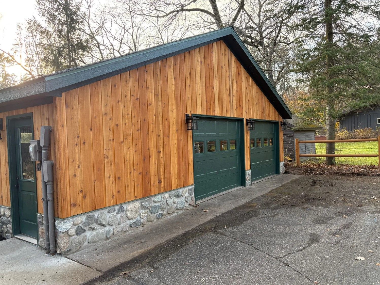 Two-car garage with green doors, wood siding, and stone base. Dark green roof.