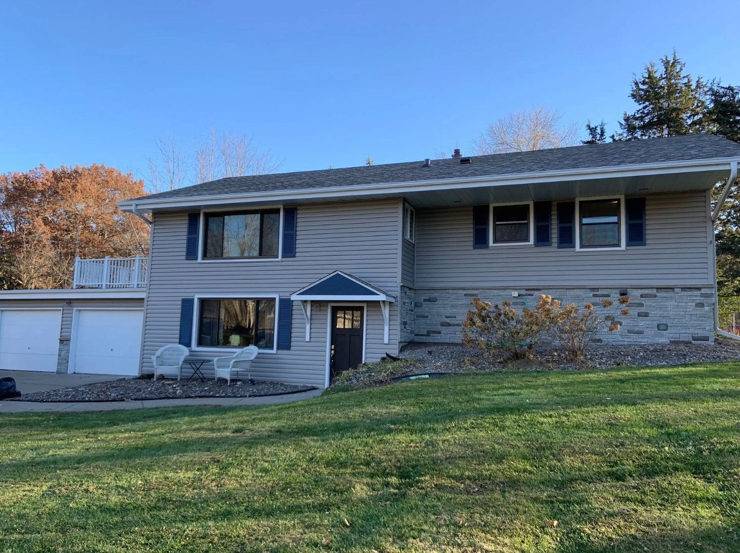 Two-story gray house with detached garage on a grassy lot under a blue sky.