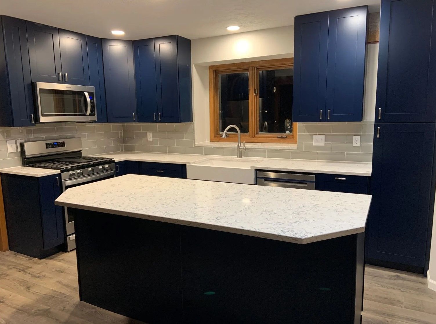 Blue kitchen with white countertops and island, stainless steel appliances, and a window above the sink.
