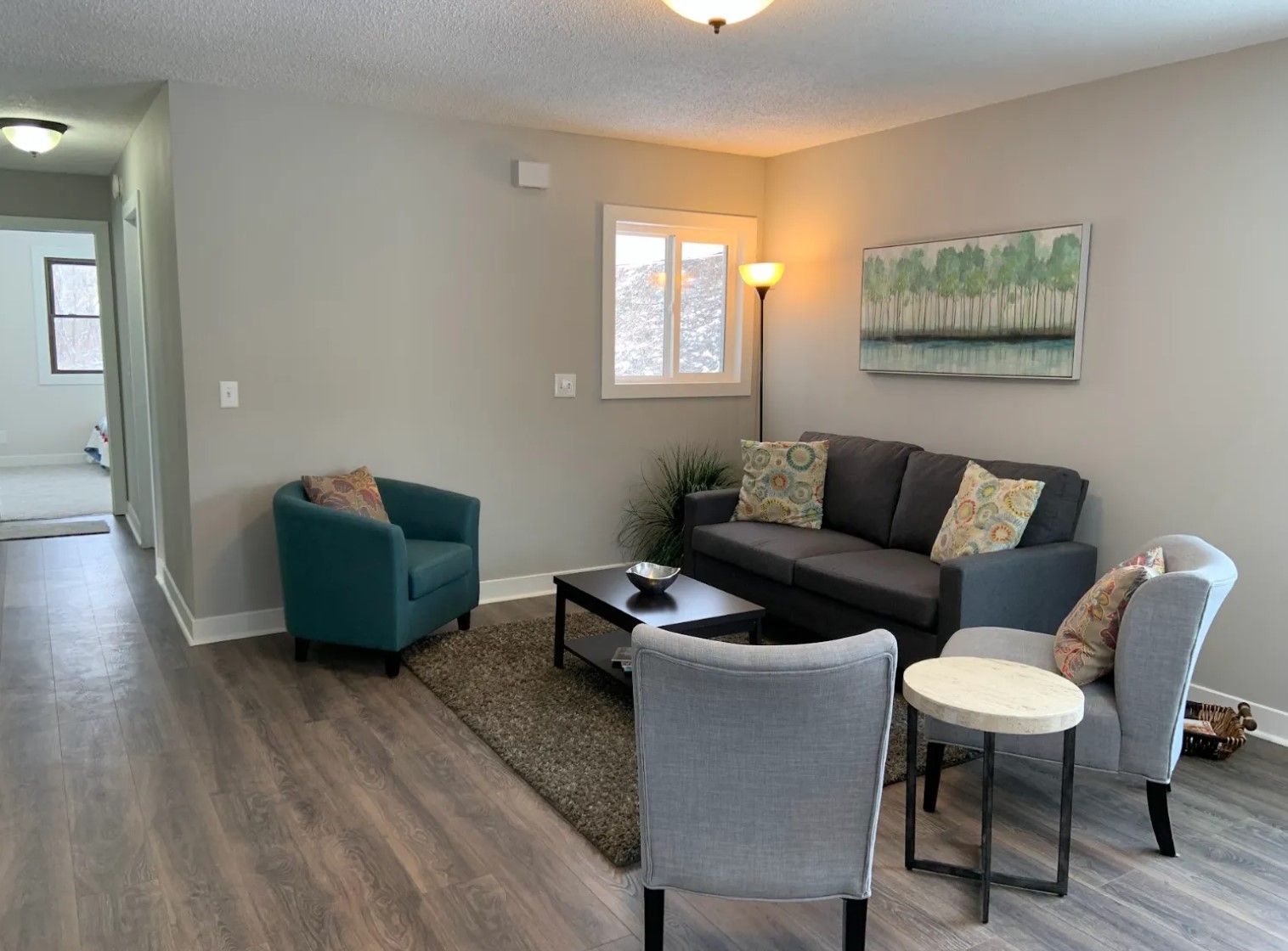 Living room with gray walls, dark gray sofa, teal armchair, and gray chairs.