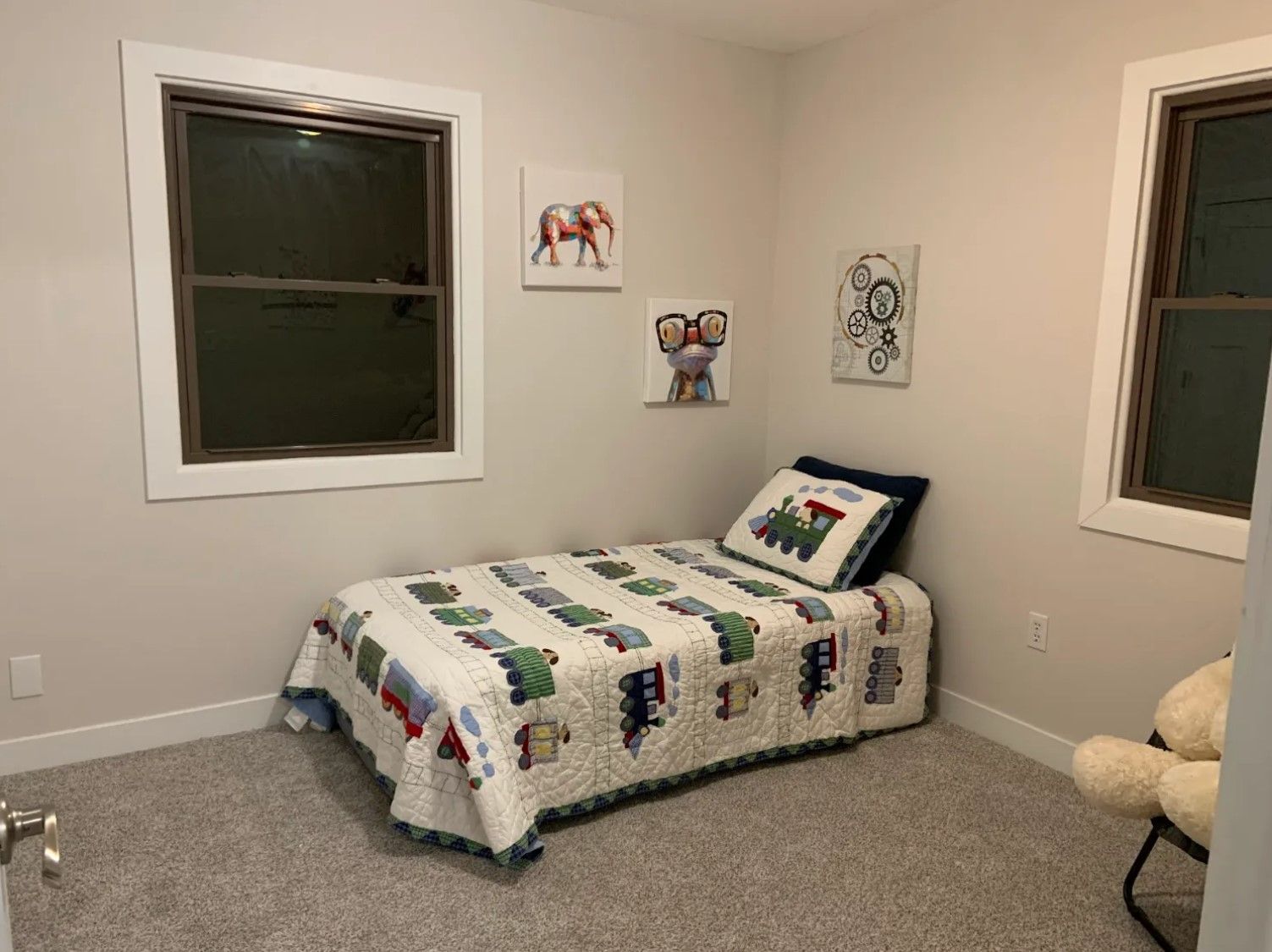 A child's bedroom with a single bed, art on the walls, and two windows.