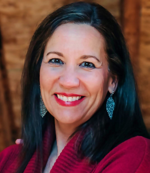 A smiling person with long dark hair, wearing red clothing and patterned silver earrings, against a textured background.