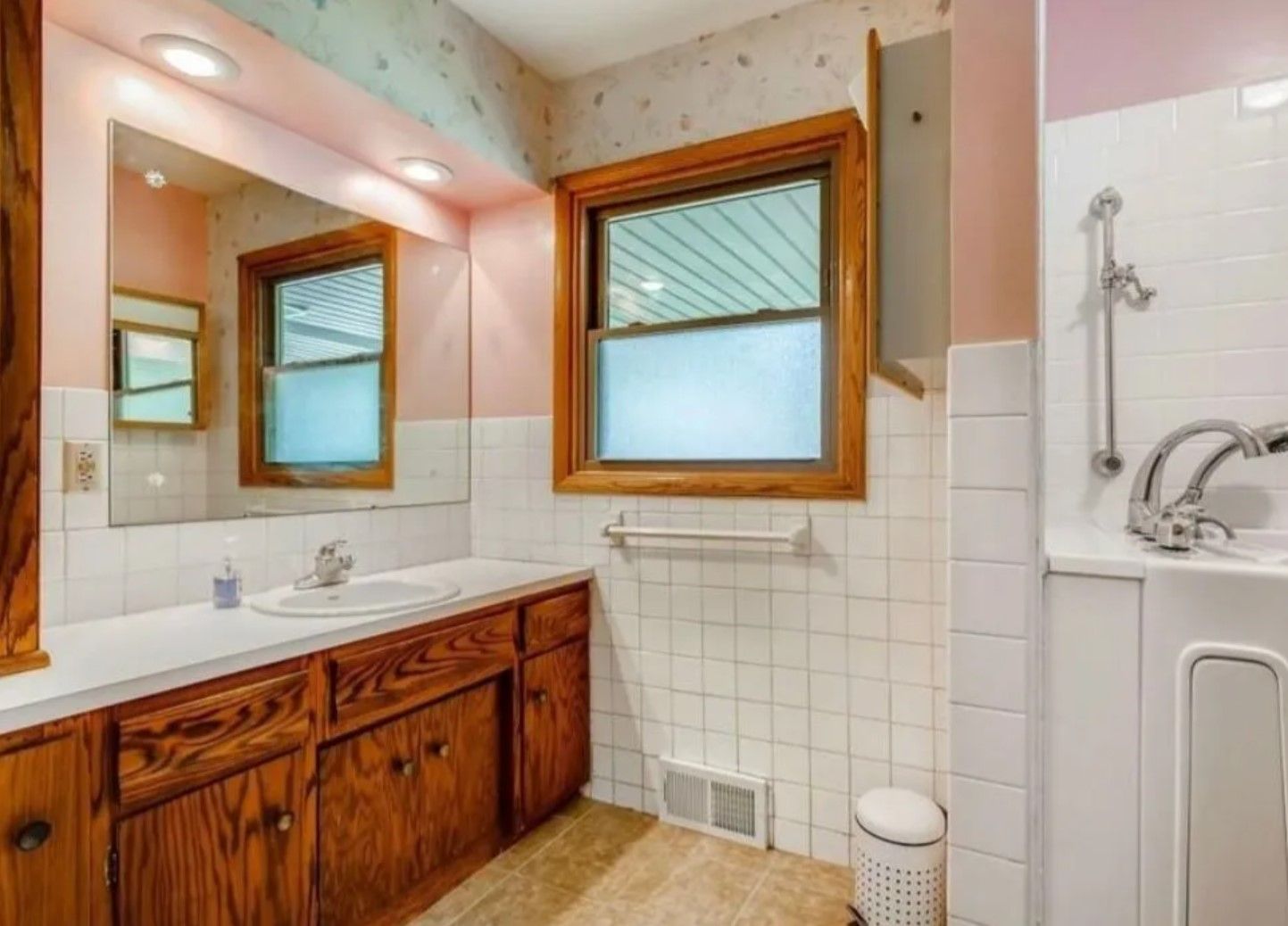 Bathroom with wood vanity, white tile, window, and a shower with a grab bar.