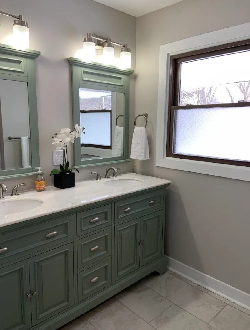 Green vanity with marble top in a bathroom with frosted window and silver fixtures.