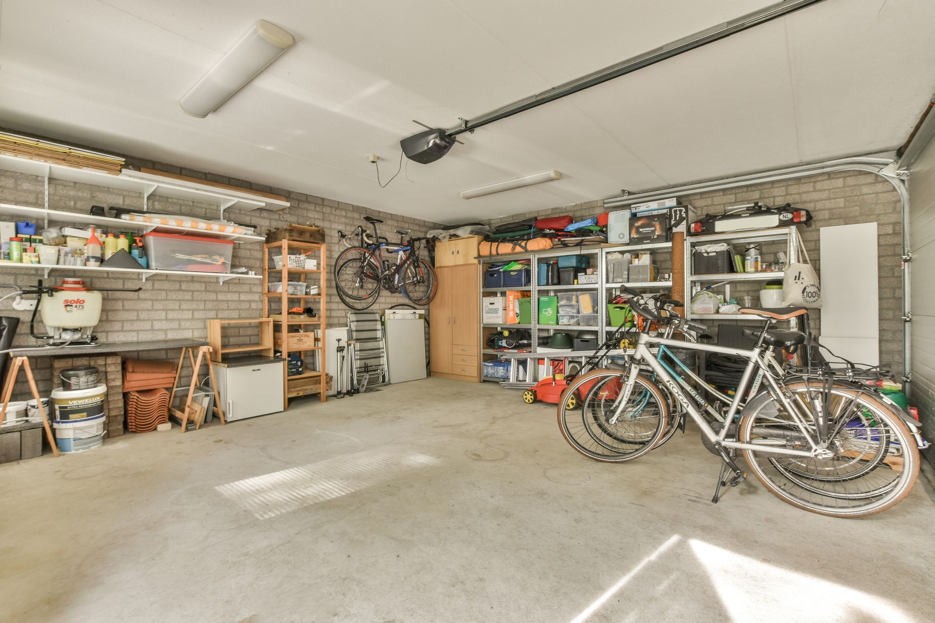 Garage interior with bicycles, shelves holding various items, and a closed garage door.