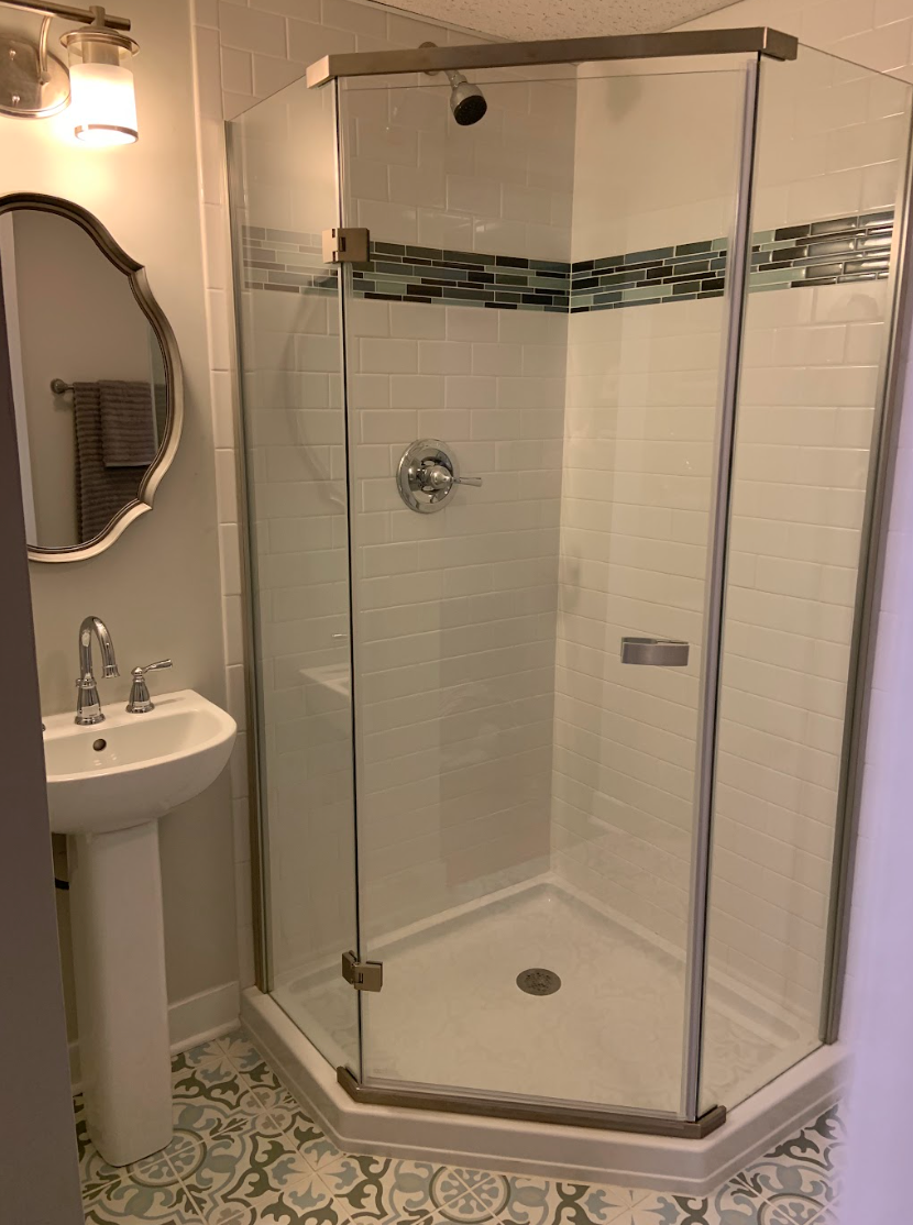 Bathroom with a pedestal sink, a hexagonal glass shower, and patterned floor tiles.