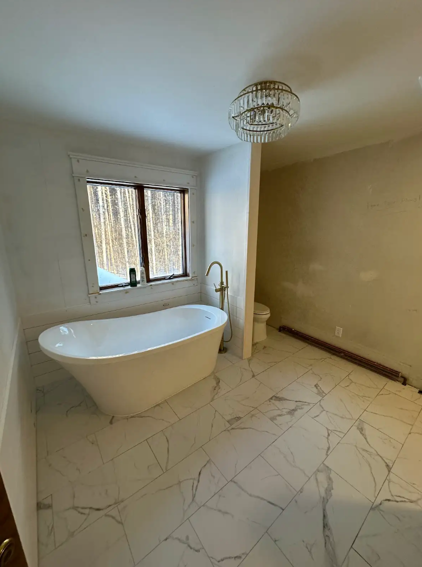 Bathroom with white tub, marble floor, chandelier, and a toilet partially visible.