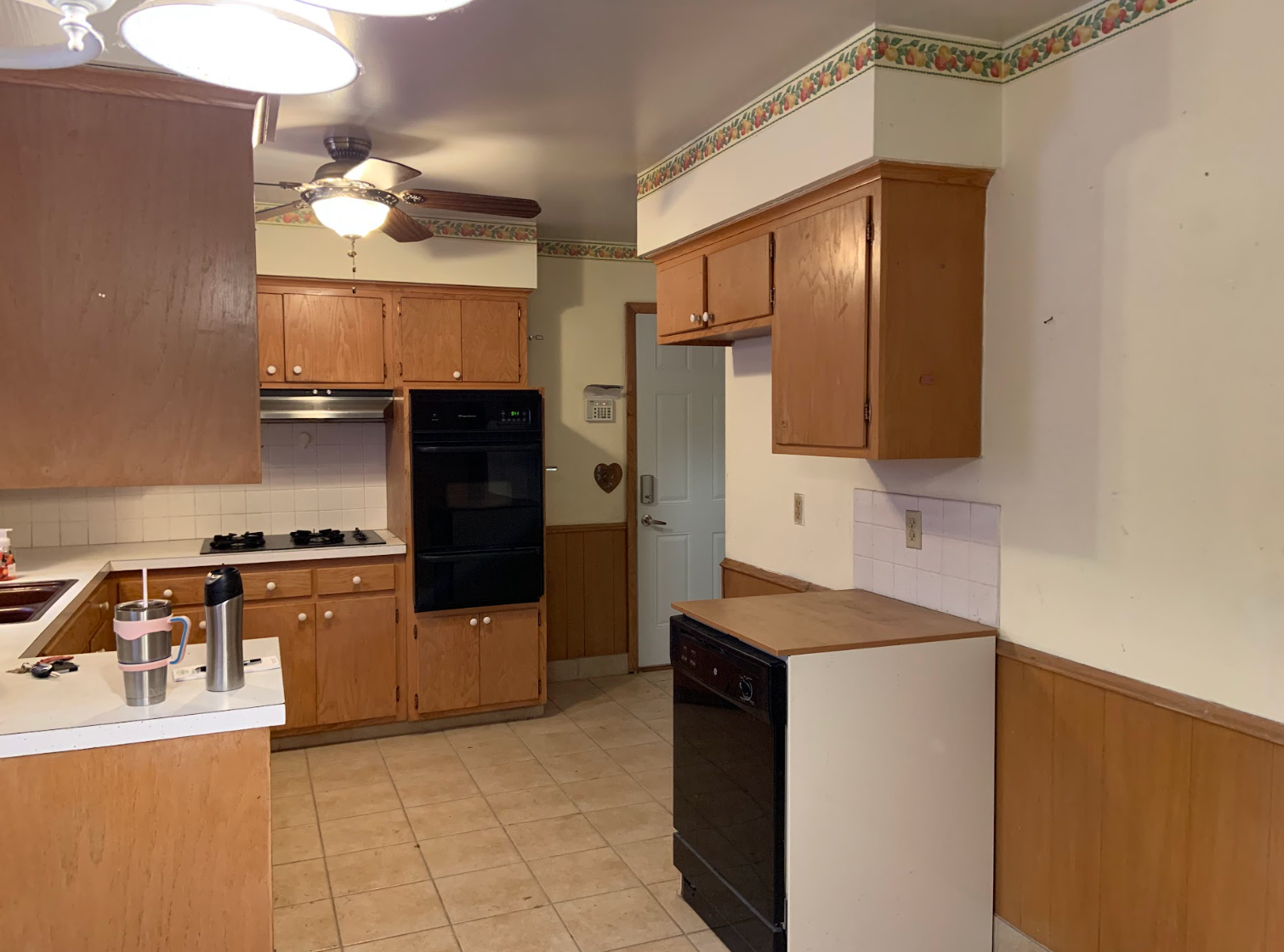 Kitchen with wood cabinets, black appliances, and tan tile floor.