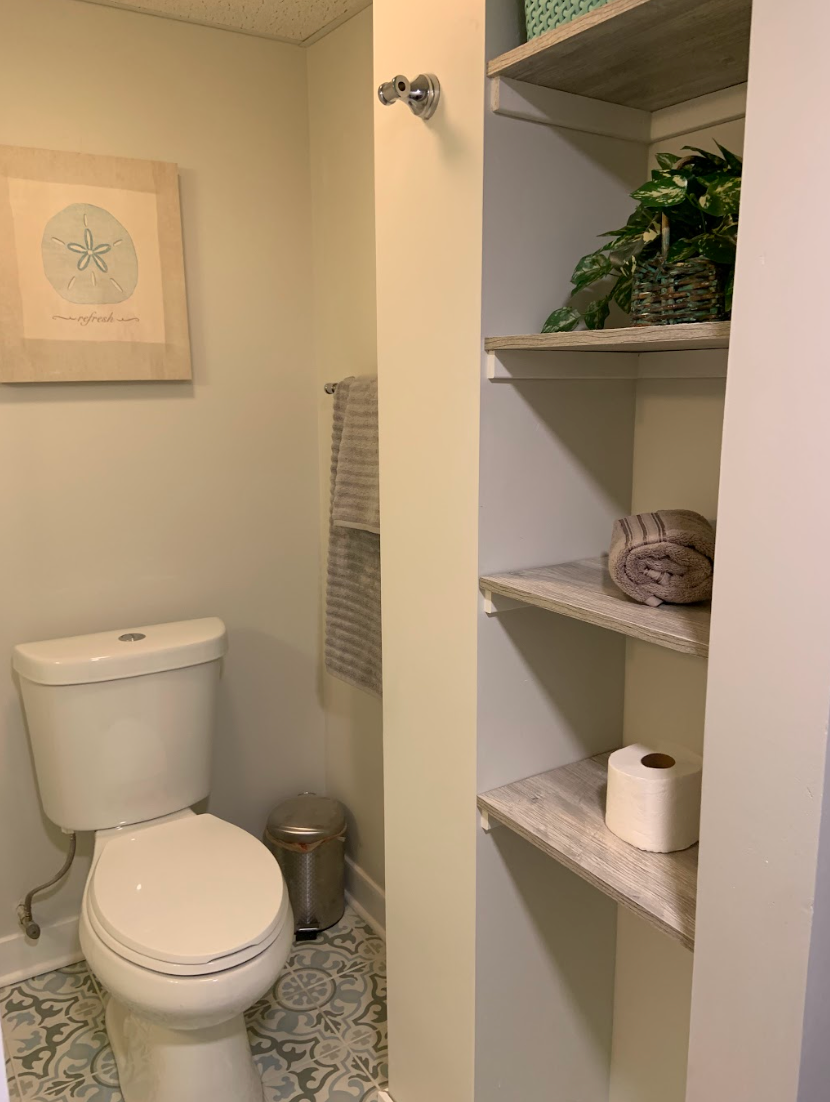 Bathroom interior with toilet, shelves, and decorative items. Light green walls, patterned floor.