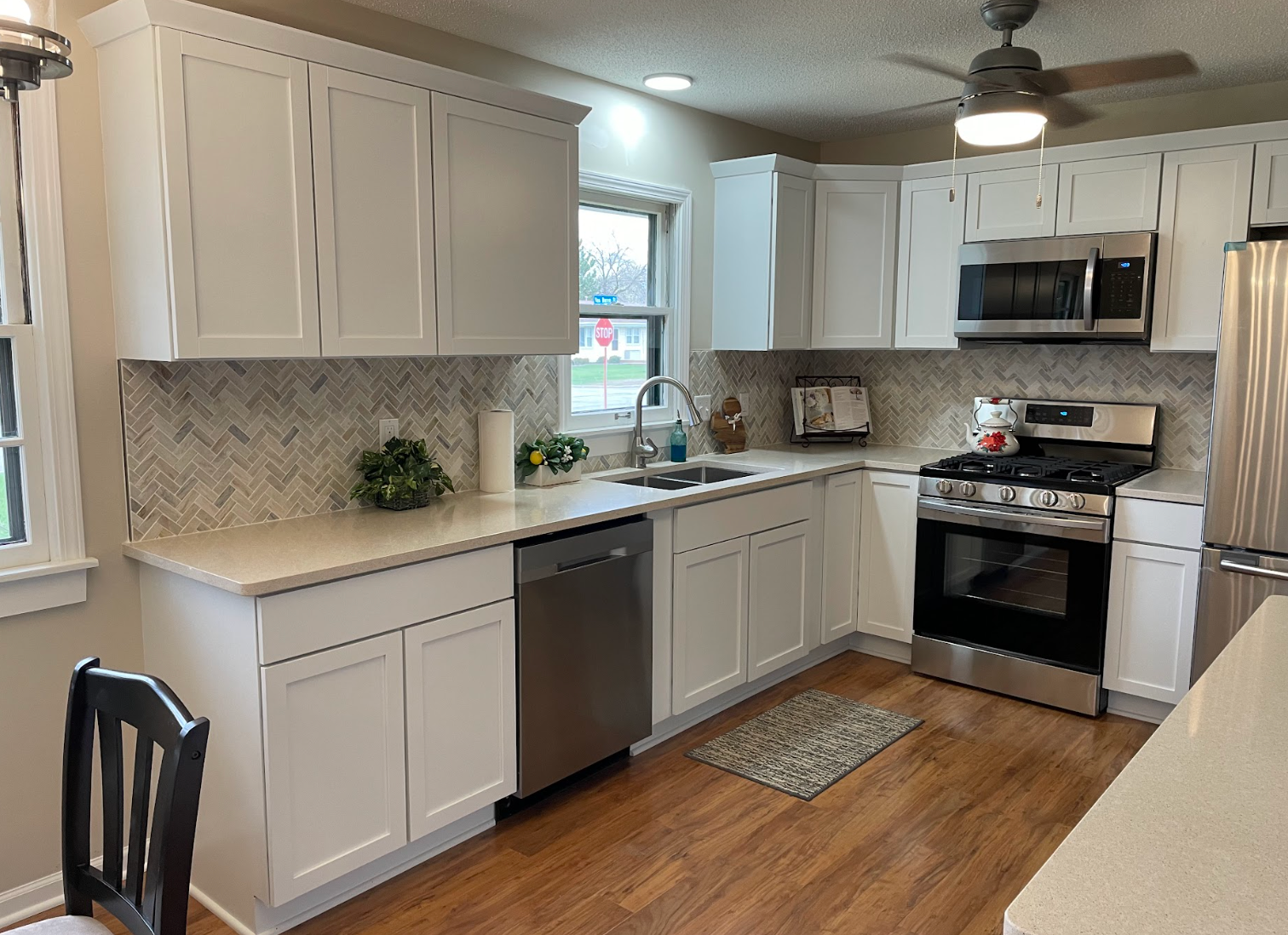 White kitchen with stainless steel appliances, herringbone backsplash, and wood floor.